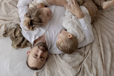 Portrait of father lying on bed with his two children relaxing - GMLF00120