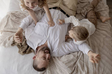 Father lying on bed playing with his two children - GMLF00121