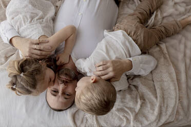 Porträt eines auf dem Bett liegenden Vaters, der von seinen beiden Kindern geküsst wird - GMLF00123