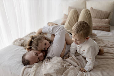 Father lying on bed spending time with his two children - GMLF00124