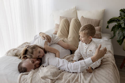 Father lying on bed cuddling with his two children stock photo