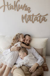 Familienporträt eines glücklichen Vaters und seiner beiden Kinder, die zu Hause kuscheln - GMLF00129