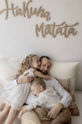 Family portrait of happy father and his two children cuddling at home - GMLF00129