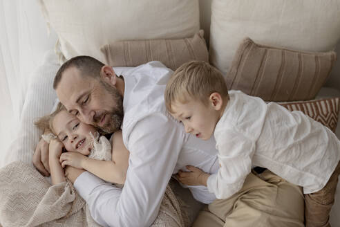 Familienporträt eines glücklichen Vaters und seiner beiden Kinder, die zu Hause kuscheln - GMLF00130