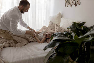 Father tickling his little daughter lying on bed - GMLF00134