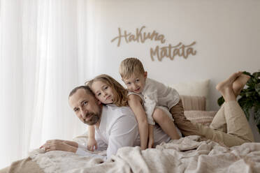 Familienporträt eines Vaters und seiner beiden Kinder, die zusammen auf einem Bett mit einem Hund liegen - GMLF00135