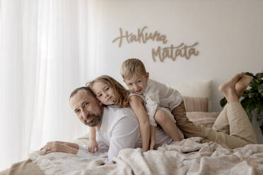 Family portrait of father and his two children lying together on bed with the dog - GMLF00135