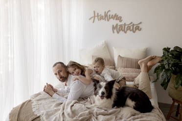 Porträt eines auf dem Bett liegenden Vaters mit seinen beiden Kindern und seinem Hund - GMLF00140