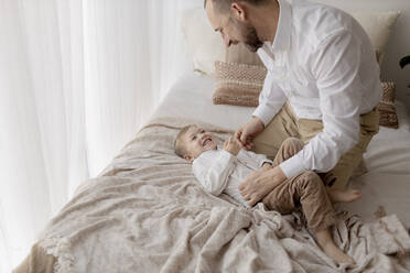 Vater hockt auf dem Bett und kitzelt seinen kleinen Sohn - GMLF00152