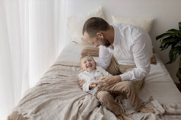 Father crouching on bed tickling his little son - GMLF00154