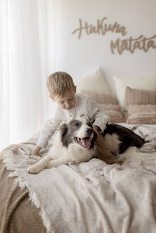 Kleiner Junge hockt auf dem Bett und streichelt seinen Hund - GMLF00162