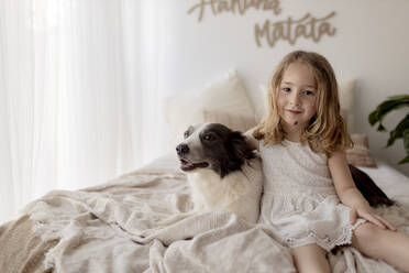 Porträt eines kleinen Mädchens auf dem Bett sitzend mit ihrem Hund - GMLF00168