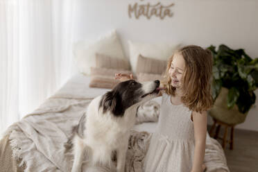 Lächelndes kleines Mädchen streichelt ihren Hund im Schlafzimmer - GMLF00169