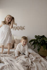 Porträt eines Jungen und seiner kleinen Schwester, die zu Hause auf dem Bett spielen - GMLF00172