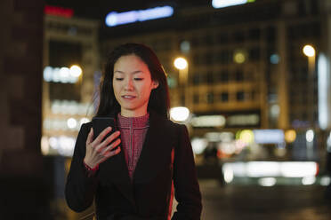 Junge Frau benutzt Smartphone in der nächtlichen Stadt, Frankfurt, Deutschland - AHSF02382