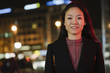 Portrait of a confident young woman in the city at night, Frankfurt, Germany - AHSF02383