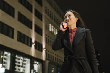 Junge Frau am Telefon in der Stadt bei Nacht, Frankfurt, Deutschland - AHSF02387
