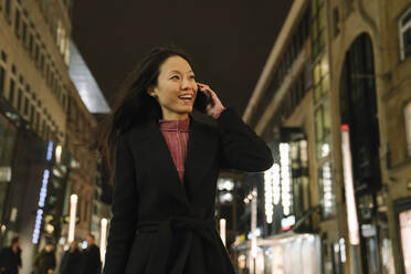 Glückliche junge Frau am Telefon in der Stadt bei Nacht, Frankfurt, Deutschland - AHSF02388