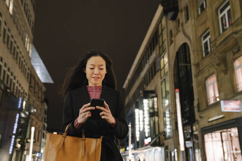 Junge Frau benutzt Smartphone in der nächtlichen Stadt, Frankfurt, Deutschland - AHSF02389
