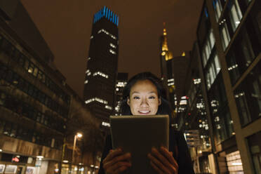 Junge Frau benutzt Tablet in der nächtlichen Stadt, Frankfurt, Deutschland - AHSF02399