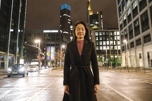 Portrait of young woman with eyes closed in the city at night, Frankfurt, Germany - AHSF02405