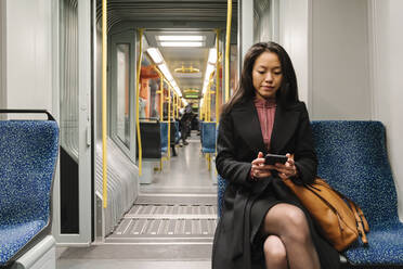 Junge Frau benutzt Smartphone in einer U-Bahn - AHSF02407