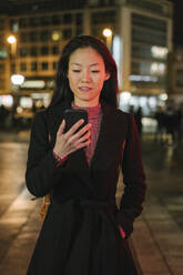 Young woman using smartphone in the city at night, Frankfurt, Germany - AHSF02412