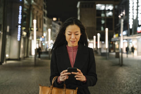 Junge Frau benutzt Smartphone in der nächtlichen Stadt, Frankfurt, Deutschland - AHSF02415