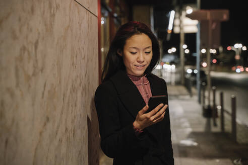 Young woman using smartphone in the city at night, Frankfurt, Germany - AHSF02418