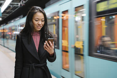 Junge Frau benutzt Smartphone in einer U-Bahn-Station - AHSF02423