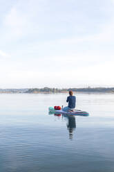 Frau, die am Morgen auf einem See auf einem Surfbrett sitzt - MMAF01301