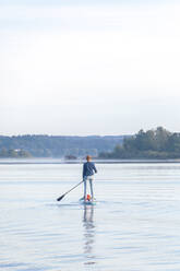 Frau, die am Morgen auf einem See auf einem Surfbrett steht - MMAF01305