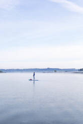 Frau, die am Morgen auf einem See auf einem Surfbrett steht - MMAF01306