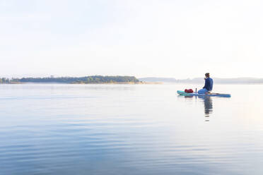 Frau sitzt morgens auf einem Surfbrett an einem See, Deutschland - MMAF01323