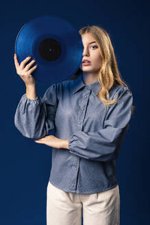 Blonde Frau mit blauer Schallplatte vor blauem Hintergrund - AGGF00055