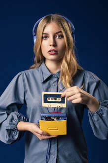Young blond woman with walkman and headphones in front of blue background - AGGF00056