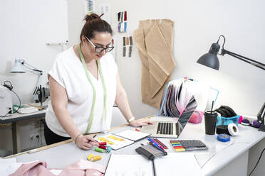 Seamstress drawing in front of a laptop working in tailor shop - VPIF02358