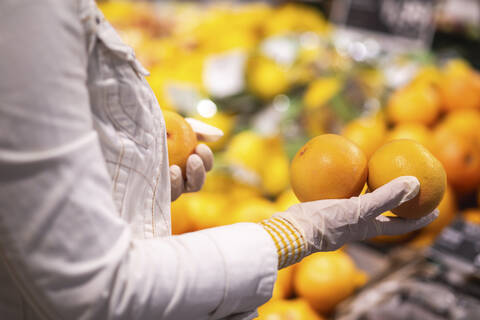 Hände mit Schutzhandschuhen halten Orangen, Nahaufnahme, lizenzfreies Stockfoto