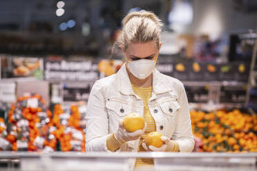 Teenage girl wearing protectice mask and gloves choosing fruits at supermarket - ASCF01255