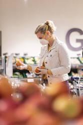 Teenage girl wearing protectice mask and gloves choosing apples at supermarket - ASCF01257