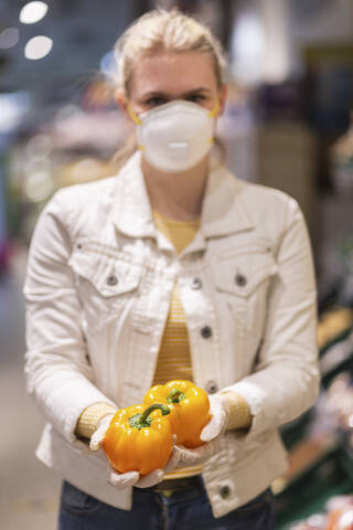 Jugendliches Mädchen mit Schutzmaske und Handschuhen, das gelbe Paprikaschoten hält, lizenzfreies Stockfoto