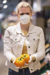 Teenage girl wearing protectice mask and gloves holding yellow bell peppers - ASCF01259