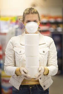 Teenager mit Schutzmaske und Handschuhen hält einen Stapel von vier Toilettenrollen im Supermarkt - ASCF01263