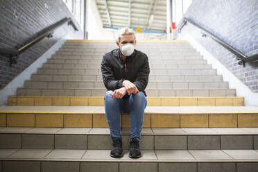 Jugendliches Mädchen mit Schutzmaske und Handschuhen auf der Treppe eines Bahnhofs sitzend - ASCF01268