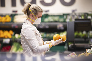 Teenage girl wearing protectice mask and gloves choosing fruits at supermarket - ASCF01269