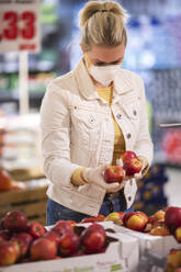 Teenage girl wearing protectice mask and gloves choosing apples at supermarket - ASCF01271