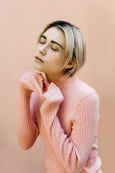 Portrait of young woman with closed eyes wearing pink turtleneck pullover in front of a pink wall - TCEF00532