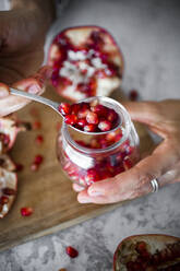 Hands of woman holding jar of pomegranate seeds - GIOF08141
