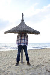 Man hiding under sunshade on the beach - ECPF00890