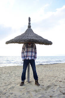 Spanien, Balearen, Palma De Mallorca, Ballermann, Mann versteckt sein Kopf unter ein Sonnenschirm am Strand von El Arenal im Winter - ECPF00890
